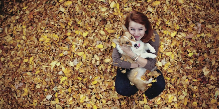 women sitting on the ground covered in fall leaves with her dog