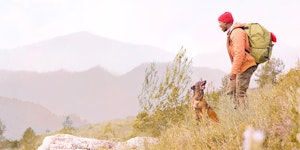 Man hiking with dog overlooking clean mountains and progress